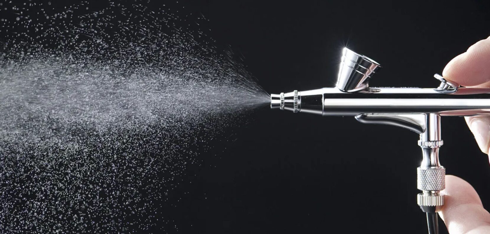 Sleek airbrush in action, releasing a fine mist of color against a black background.